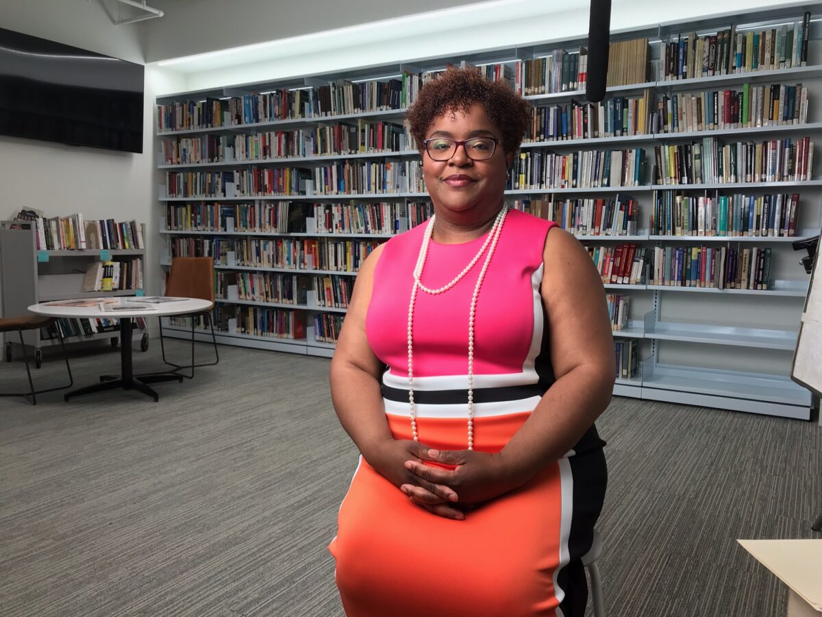 a woman in a bright professional dress sits for a portrait in front of a wall of books