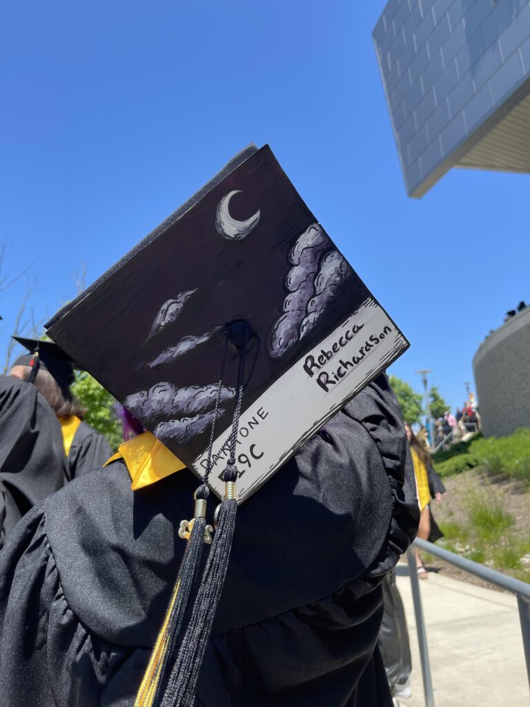A graduating student displays her cap decorated with a moon and clouds.