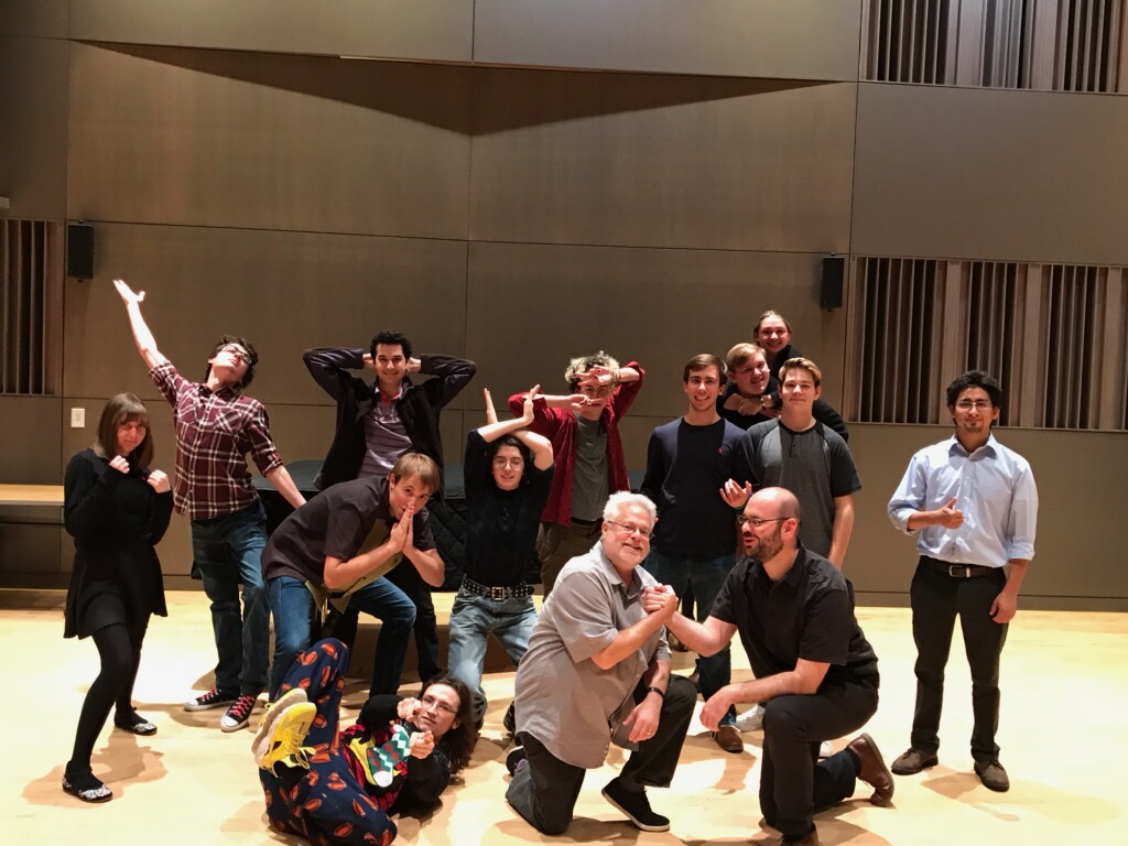 A community of performers strikes various poses on the stage. 