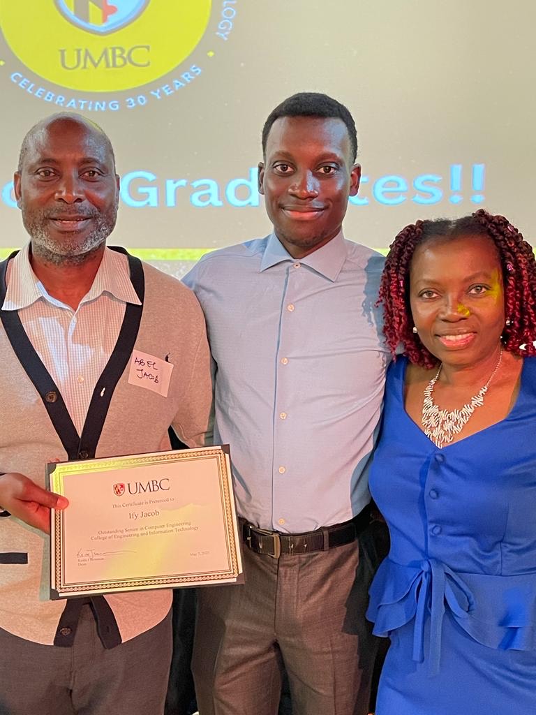 A father, son, and mother smiling in camera at awards celebration. Father is holding certificate award for Ify Jacob, his son who was a UMBC student. 