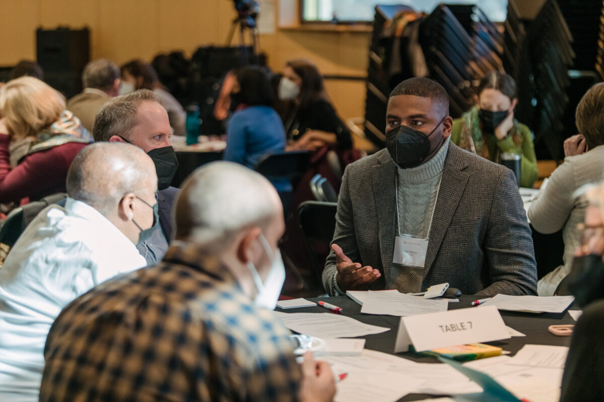 A professor leads a conversation with colleagues seated around a table.