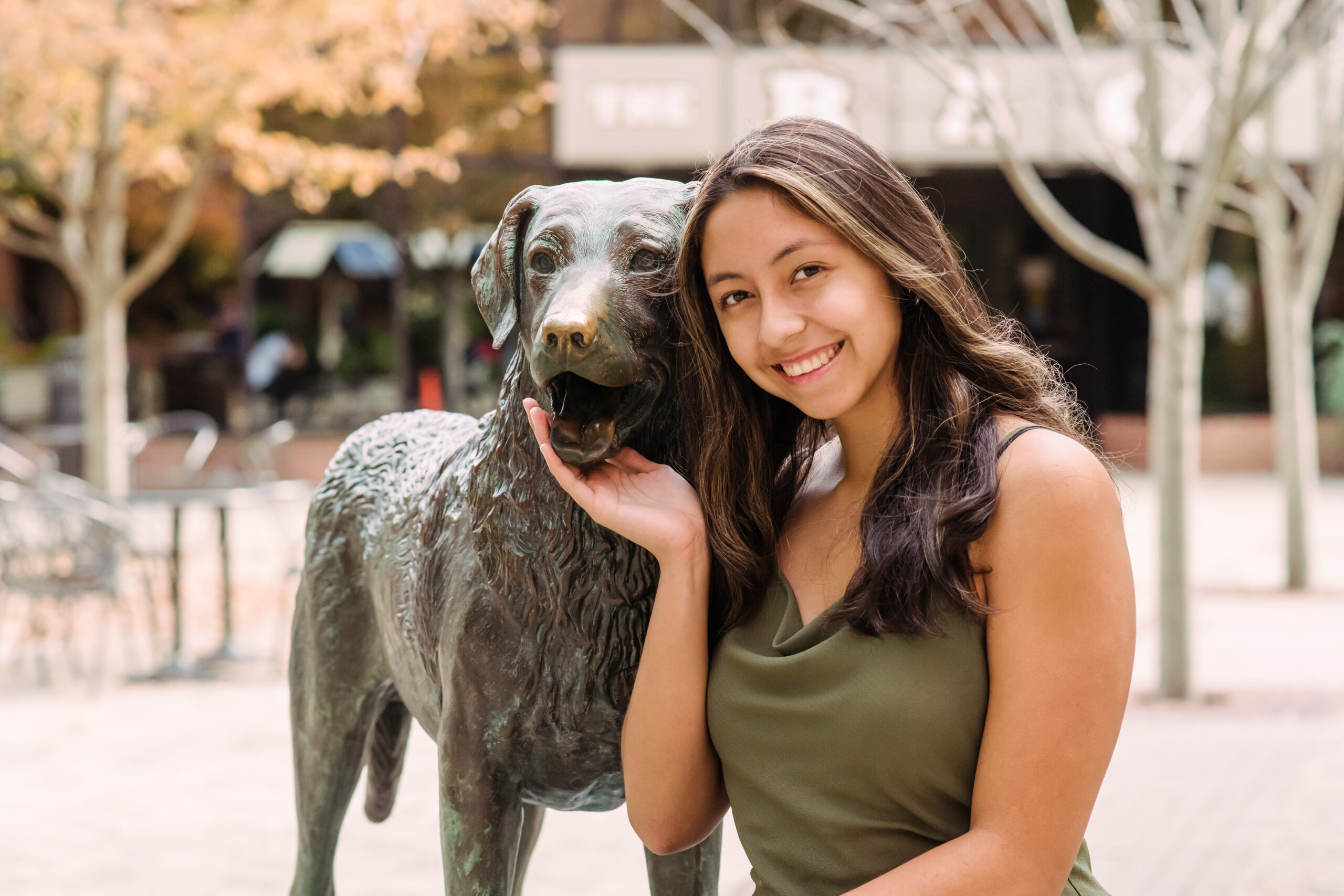 A young woman with dark hair smiles at the camera, posing with a statue of a dog