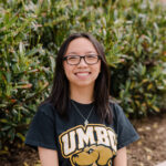 A woman wearing a UMBC t-shirt smiles at the camera