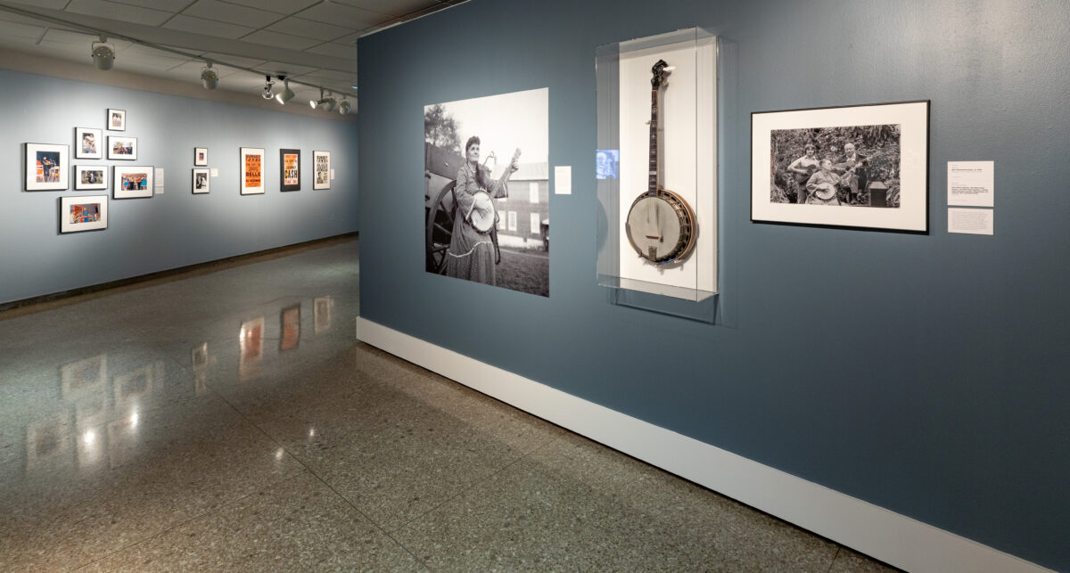 A view of a gallery exhibit showing photos and musical instruments belonging to Ola Belle Reed.