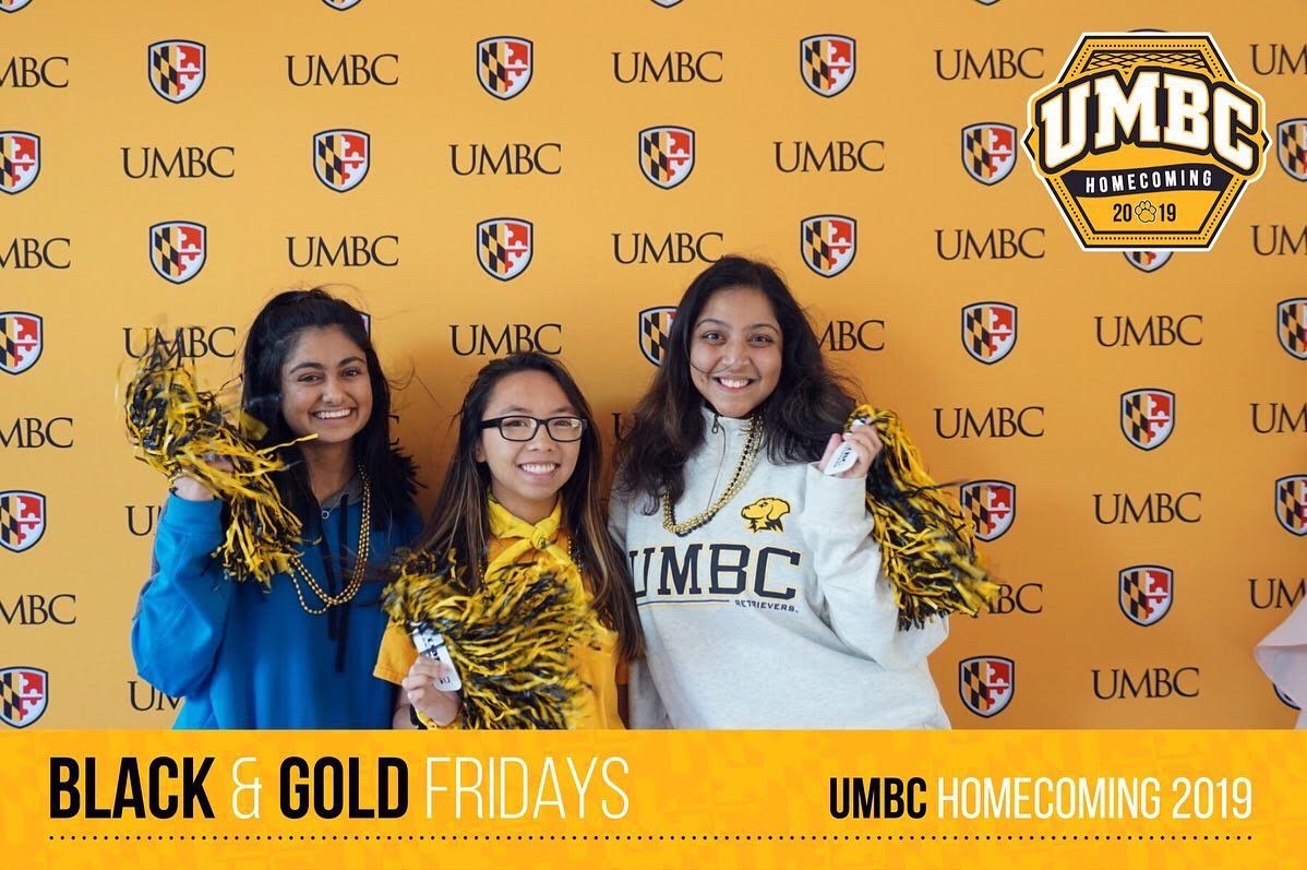 Against a gold background with the UMBC logo, three women smile at the camera