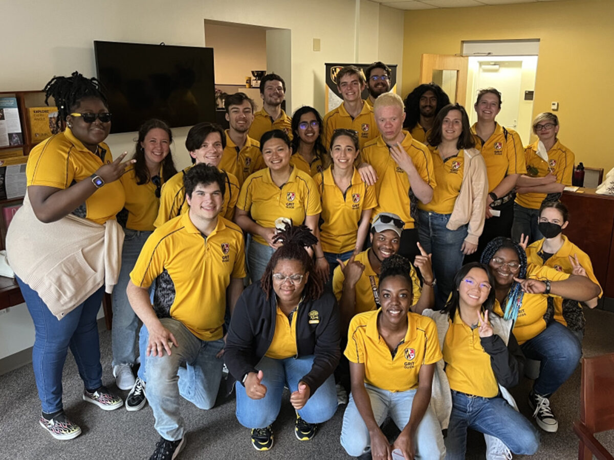 A group of people wearing gold colored shirts with "Grit Guide" logos smile at the camera