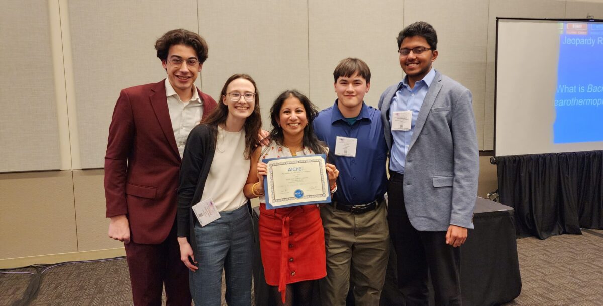 Group photo of five people in professional attire, the one in the center holding a certificate 