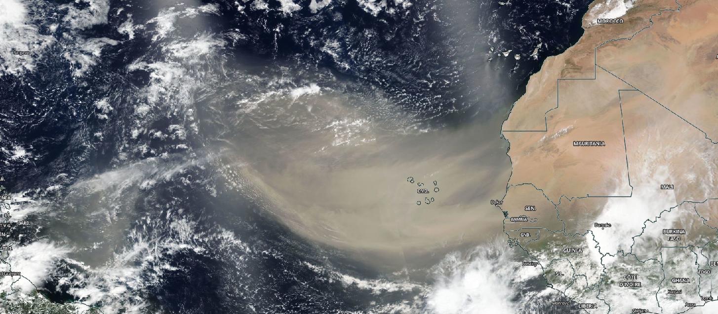 Satellite image showing Africa on the right and a large sweep of tan atmospheric dust over the Atlantic Ocean along with white and gray clouds