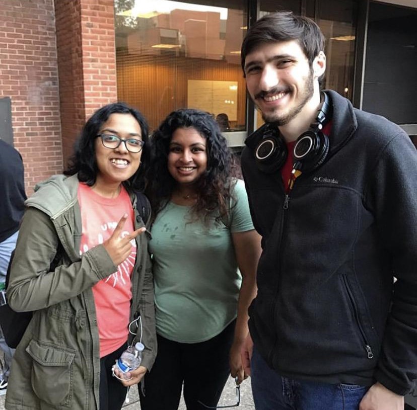 Three college friends, part of a community of support, stand close together by a brick building.