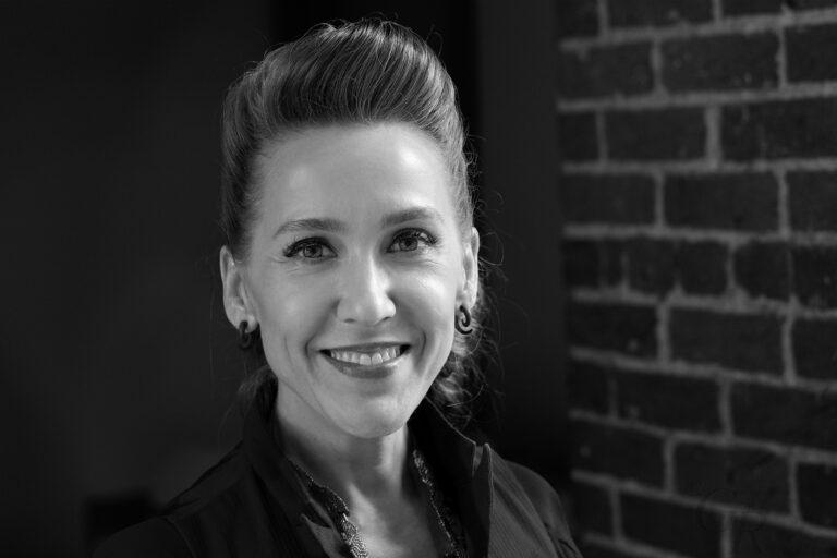 In a black and white image, a white woman smiles at the camera