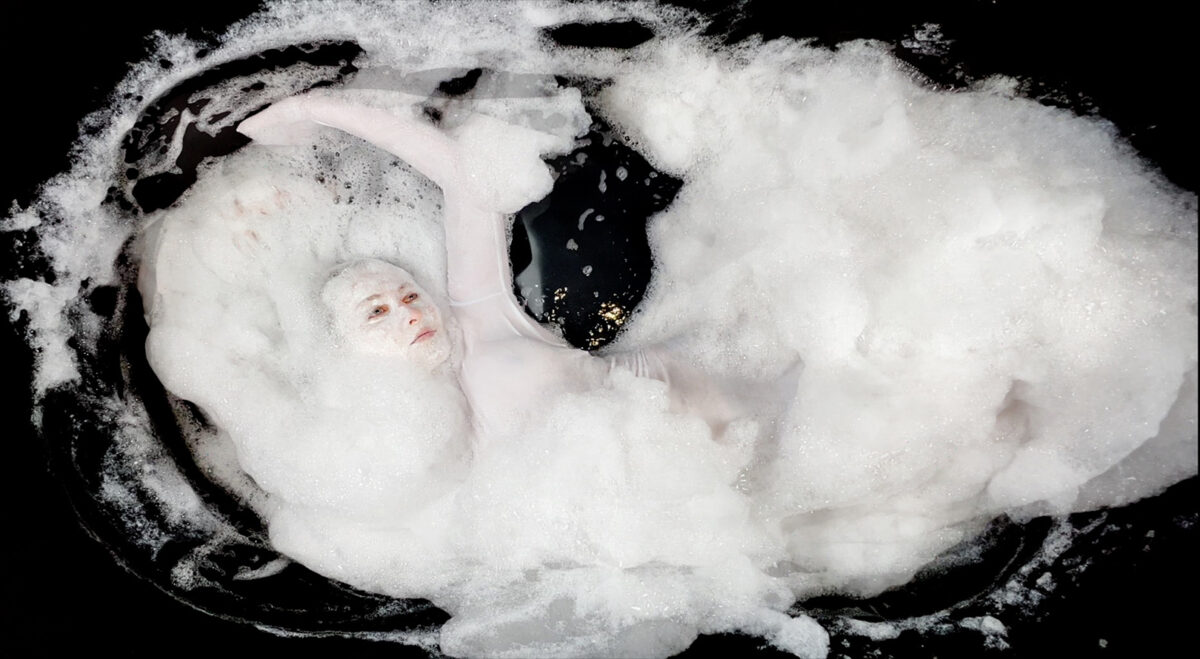 In a surrealistic looking image, a woman is in a bathtub surrounded by soap bubbles