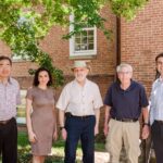 Five people stand in front of brick building and smile at camera.