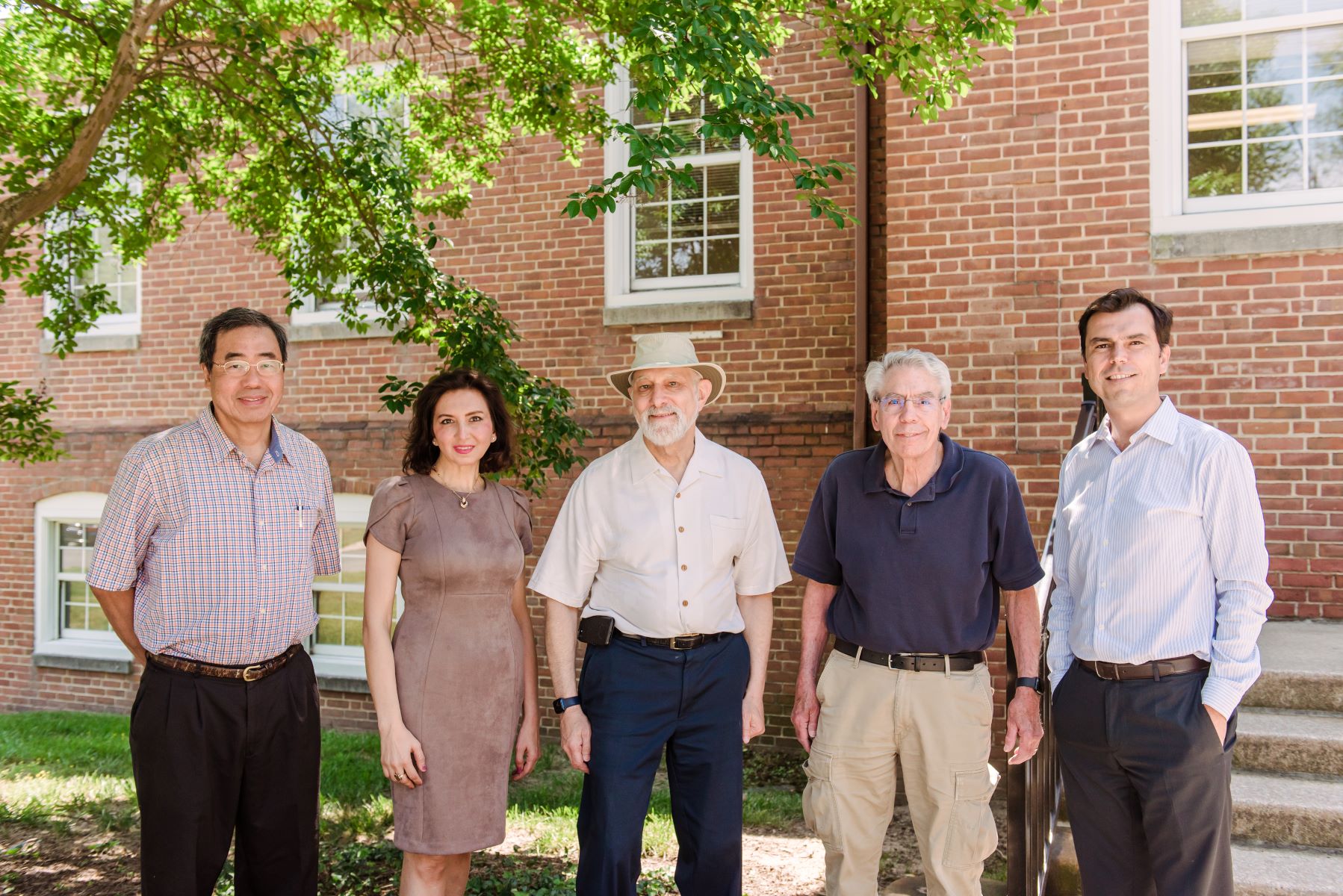 Five people stand in front of brick building and smile at camera.