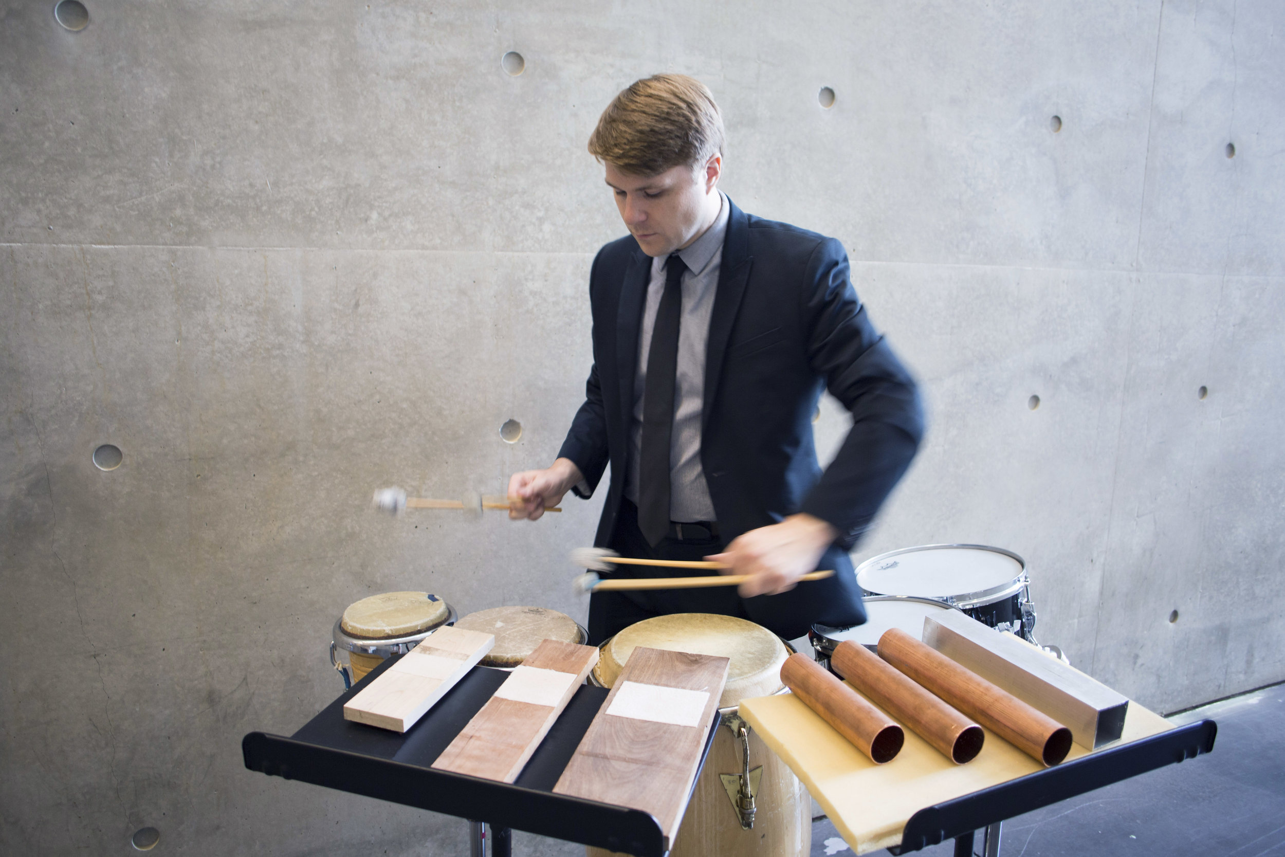 A percussionist in a dark blue suit performs on some instruments