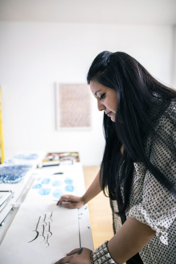 Hadieh Shafie at her desk looks at art work in a Persian script.