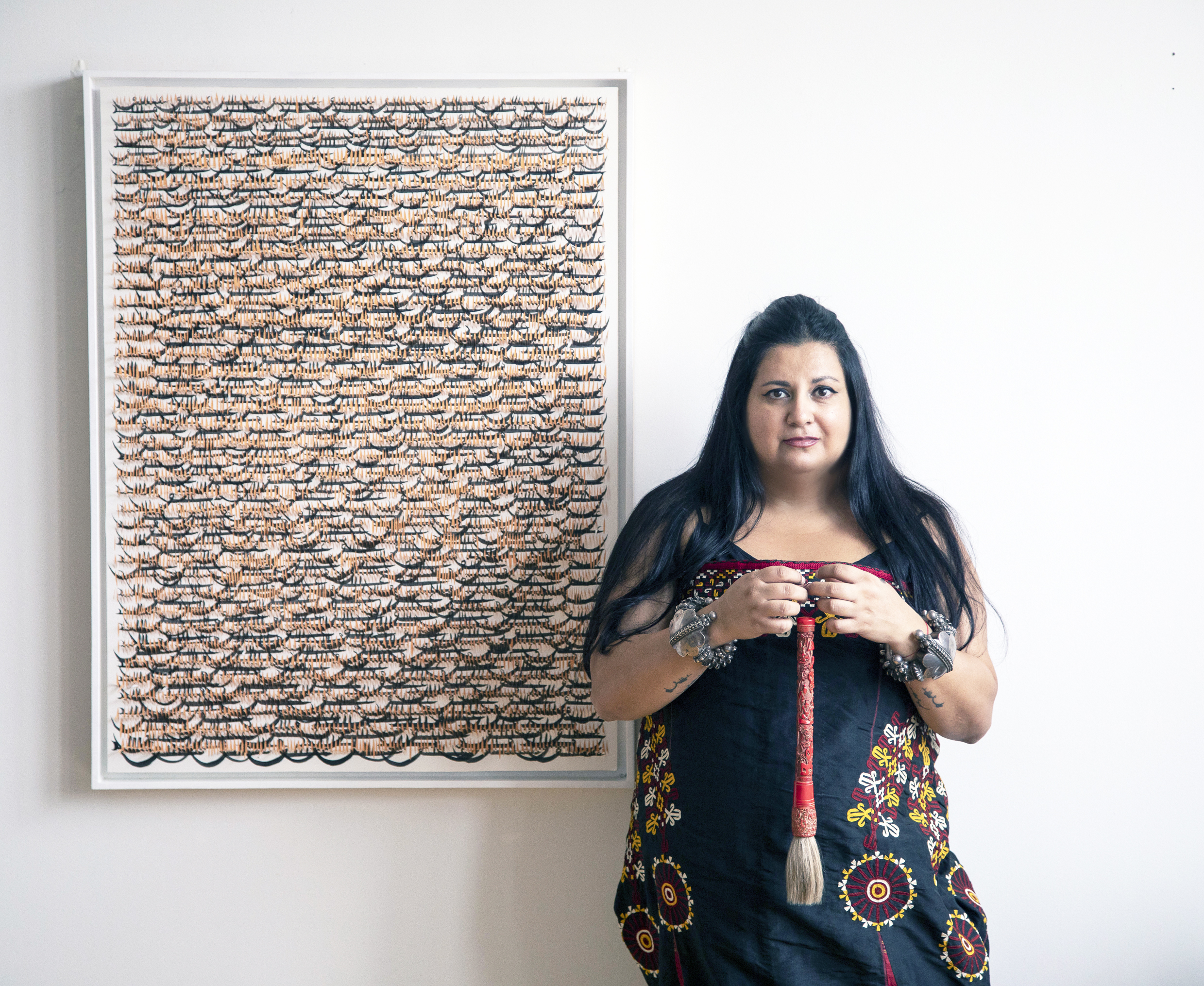 A woman with dark hair stands next to a piece of art