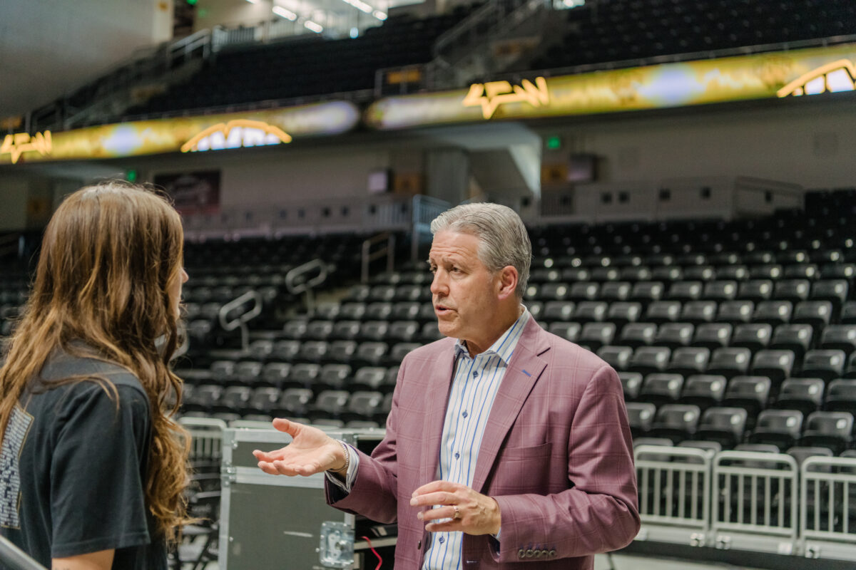 A man in a suit talks to a female athlete in an arena