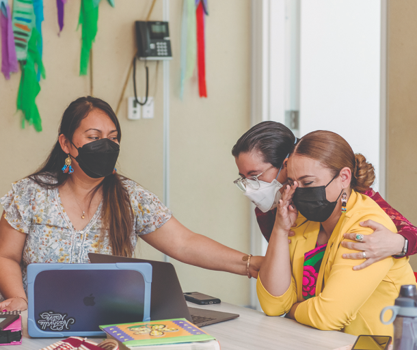 Three women in masks, sitting together and supporting someone in distress.