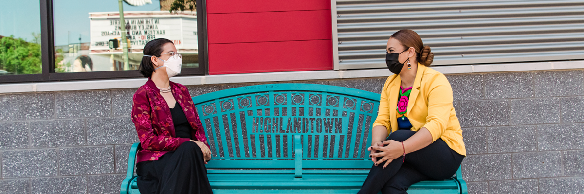 Two women sitting on a blue bench speak to each other.