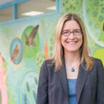 portrait of woman standing in front of colorful, science-themed mural