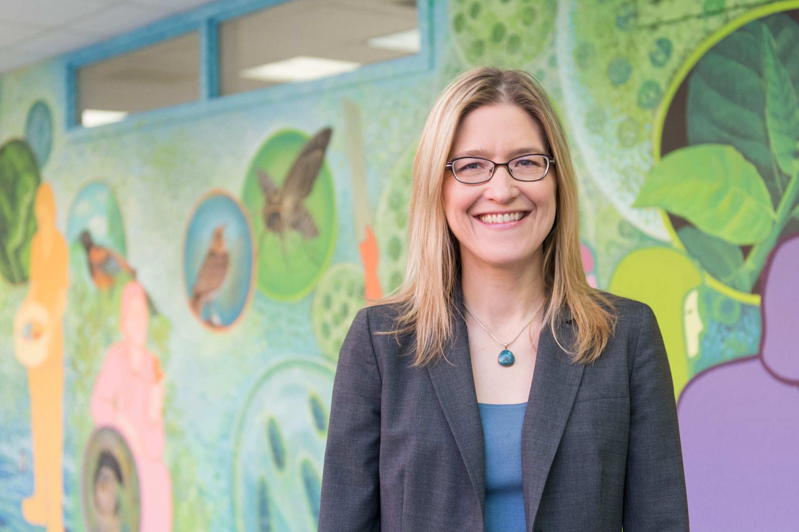portrait of woman standing in front of colorful, science-themed mural