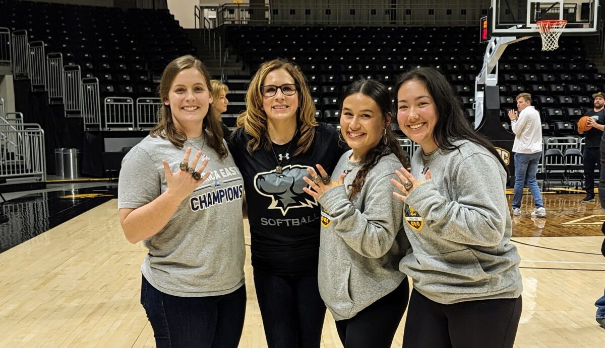 Jamie Gurganus, second from left, poses with softball players displaying their 2022 America East Championship jewelry.