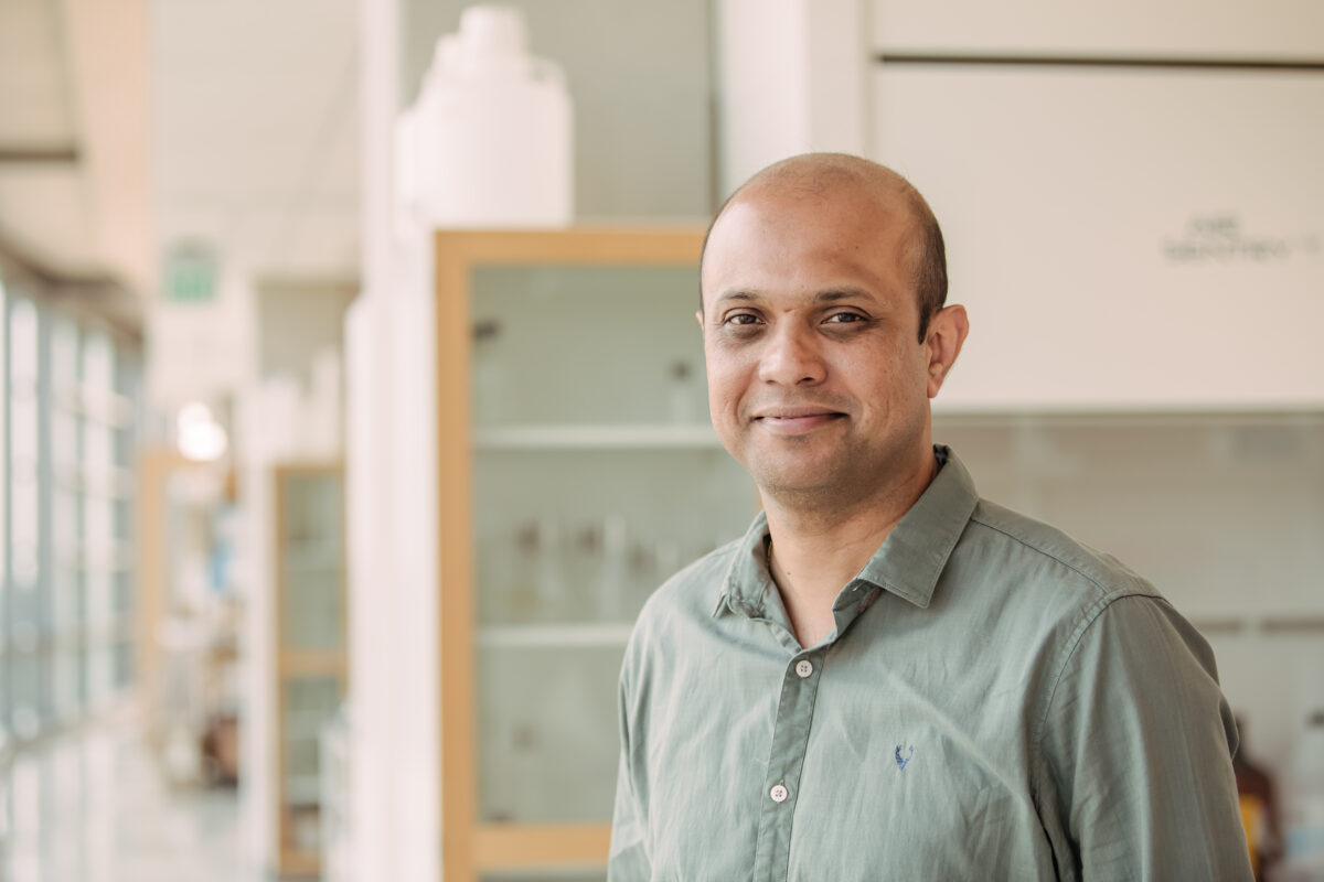 Portrait of man in sage green shirt, laboratory corridor in background