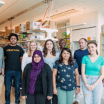 Group photo of nine people in a brightly lit laboratory