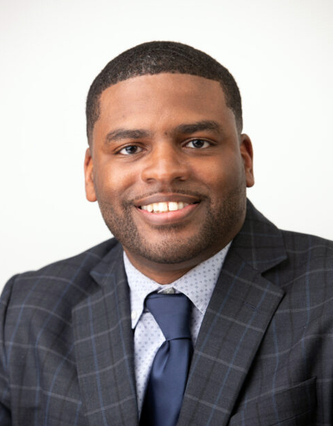 A Black man wearing a suit smiles at the camera