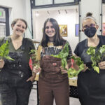 group photo of three women in overalls holding plants, indoors
