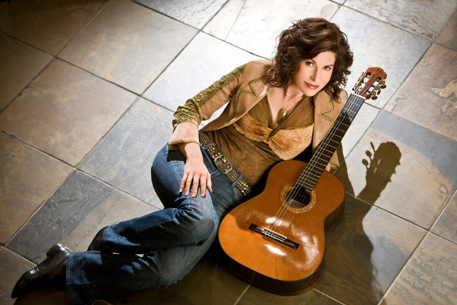 Looking up at the camera from the floor, a woman poses with a classical guitar