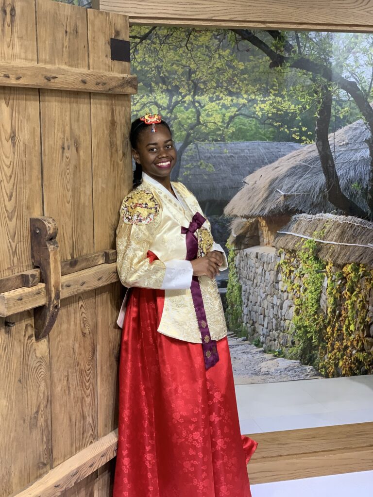 A young women poses for a picture wearing a bright red and cream hanbok, South Korean traditional clothing.