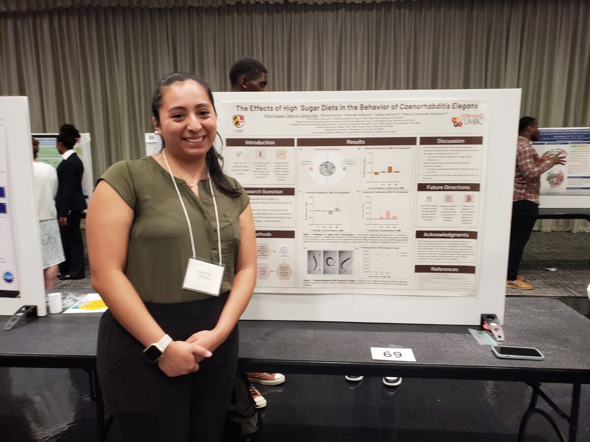 Young woman in professional attire stands next to a research poster