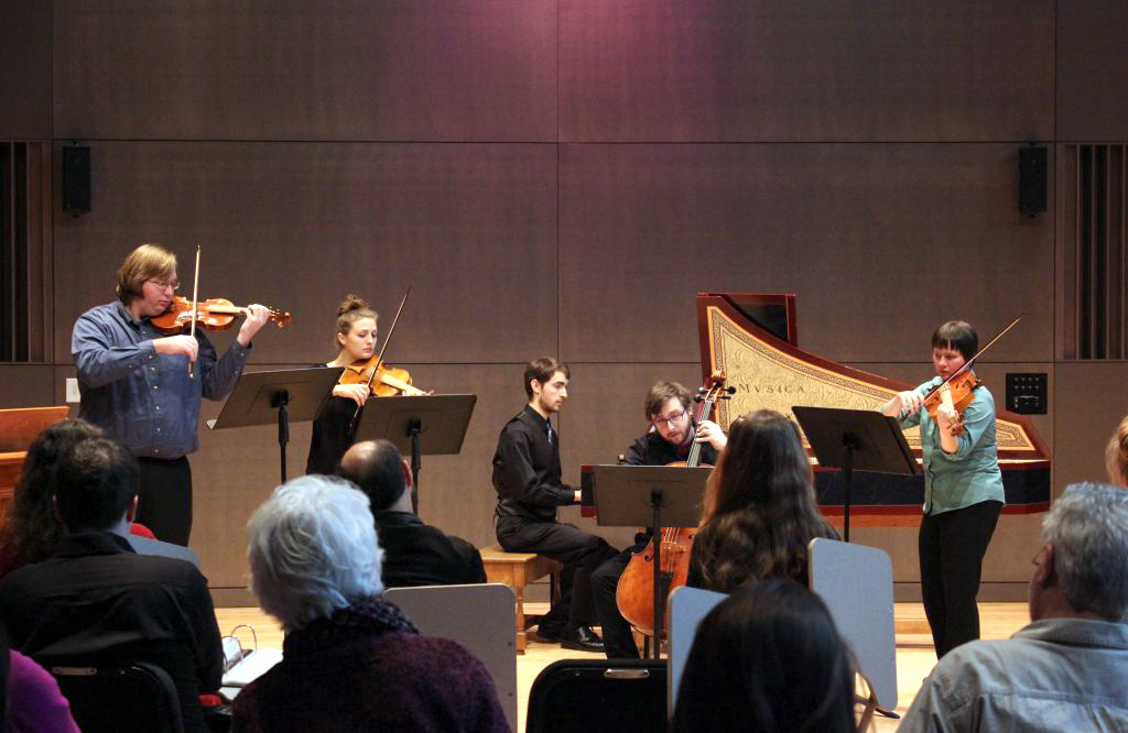 A group of five musicians perform on string instruments and a harpsichord