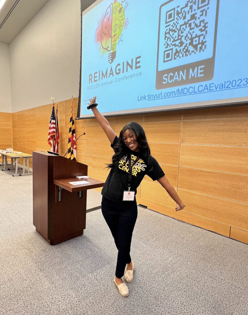 a student dressed in black poses triumphantly in front of a presentation screen