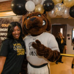 a UMBC student poses with True Grit, the live mascot with festive black and gold balloons around
