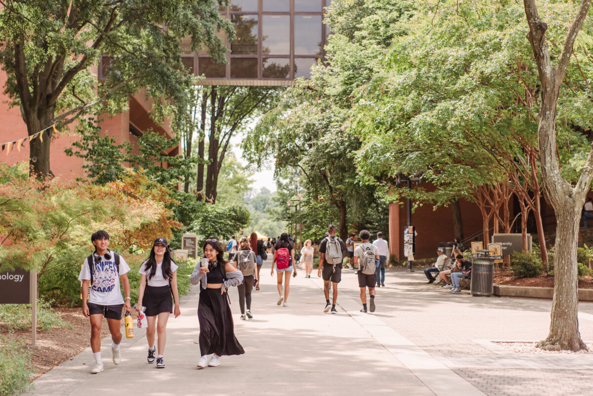 Students milling about on campus walkway with trees in the background 