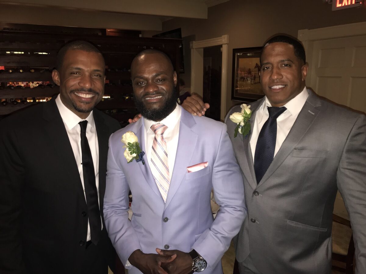 Three men in suits smile at a wedding