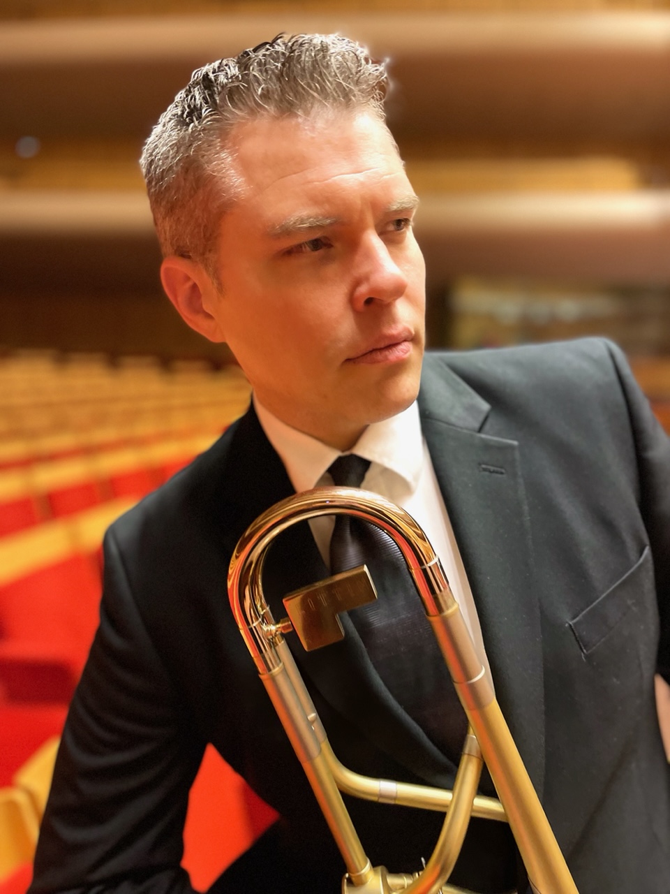 A man in a suit poses with a trombone