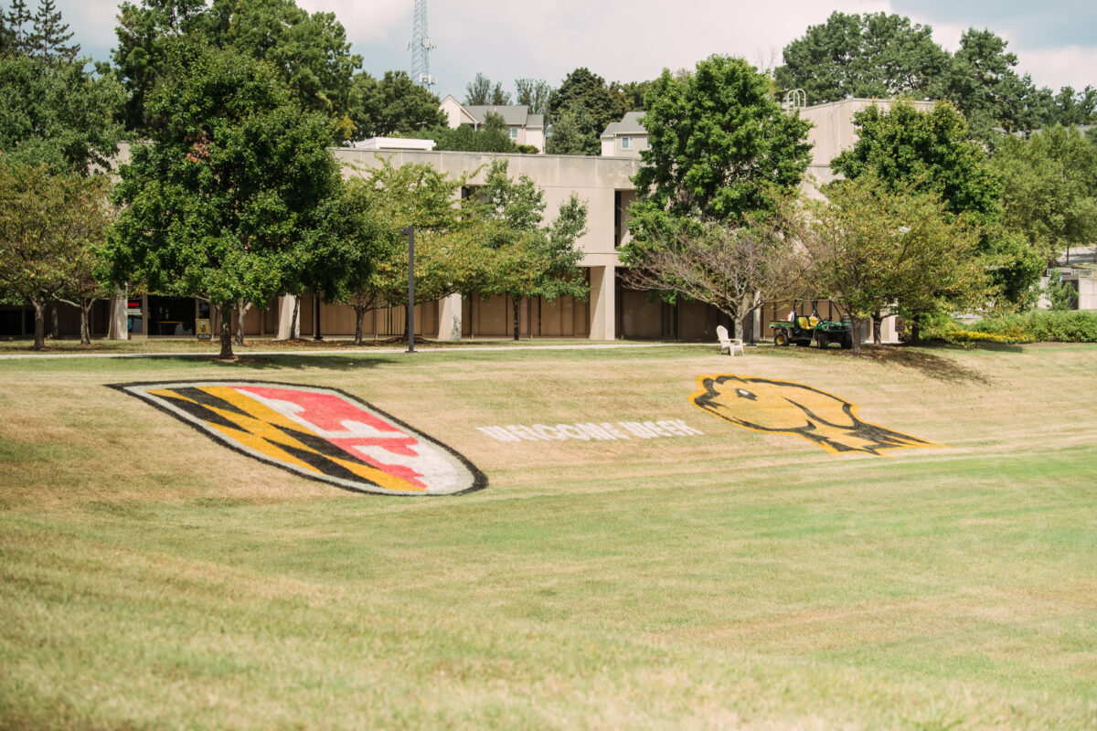 Large grassy field with UMBC logo and UMBC mascot spray painted on ground with text "Welcome Week"