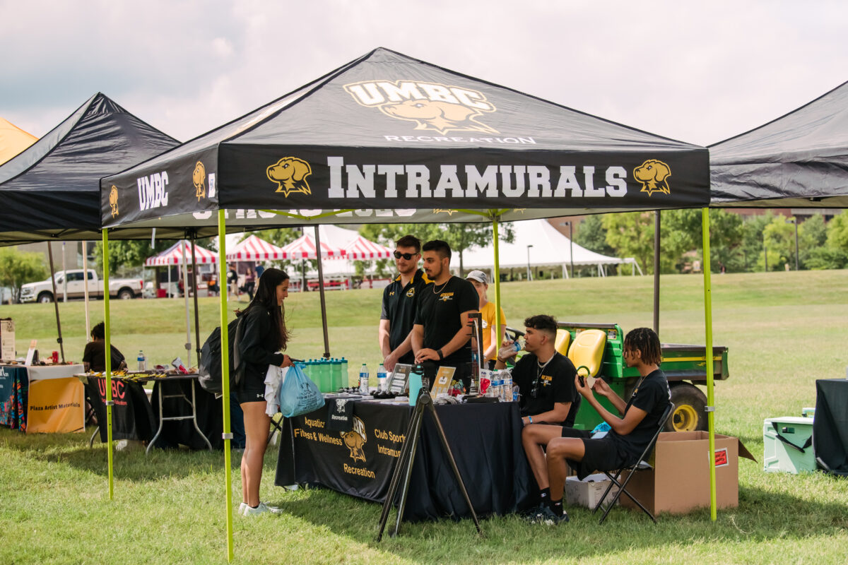 A UMBC intramural tent is set up on a field with people at the table waiting for visitors