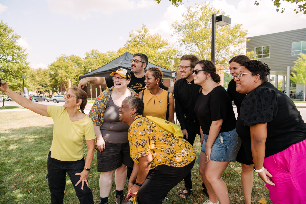 A group of individuals in black and gold smile for a selfie with UBMC's president outside