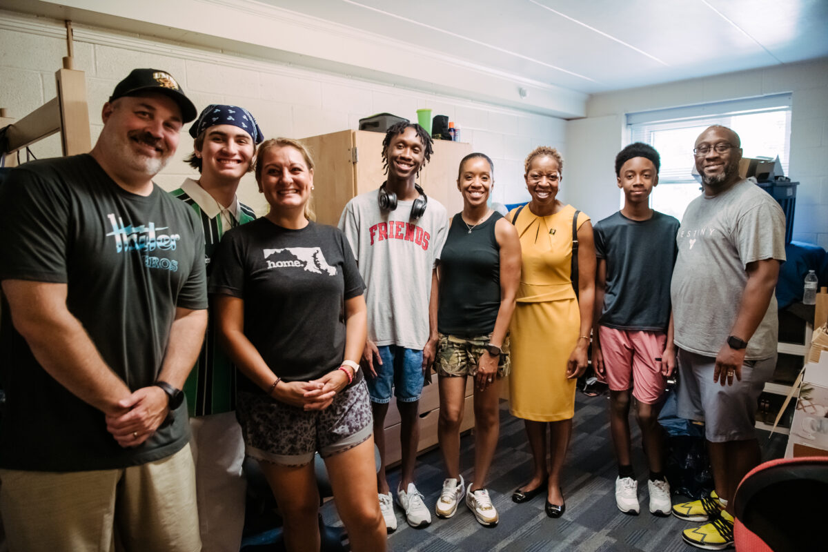 Family members gather together in a dorm room with the UMBC president for a move-in photo