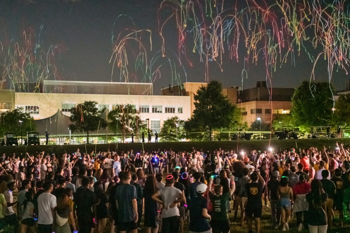 The aftermath of brightly-colored fireworks fall down the sky while a crowd looks on