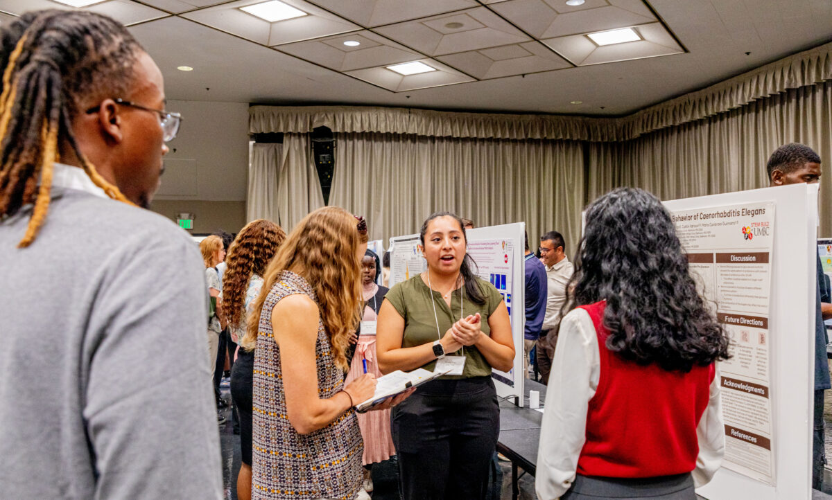 a group of three people in discussion between rows of research posters in a high-ceilinged ballroom