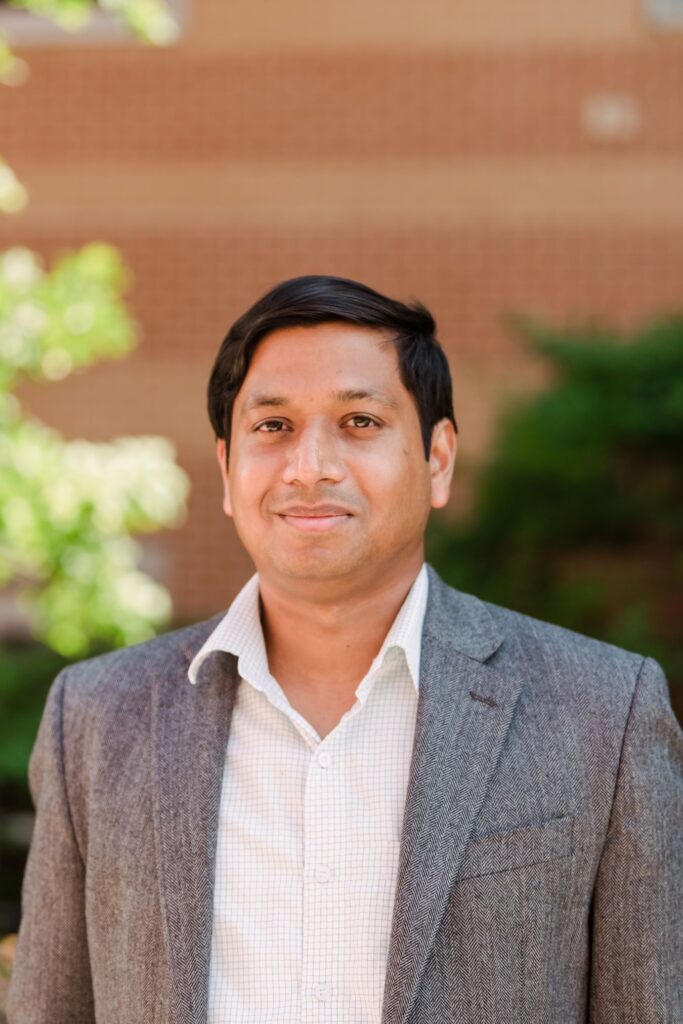 Portrait photo of man in suit jacket in front of a brick building.