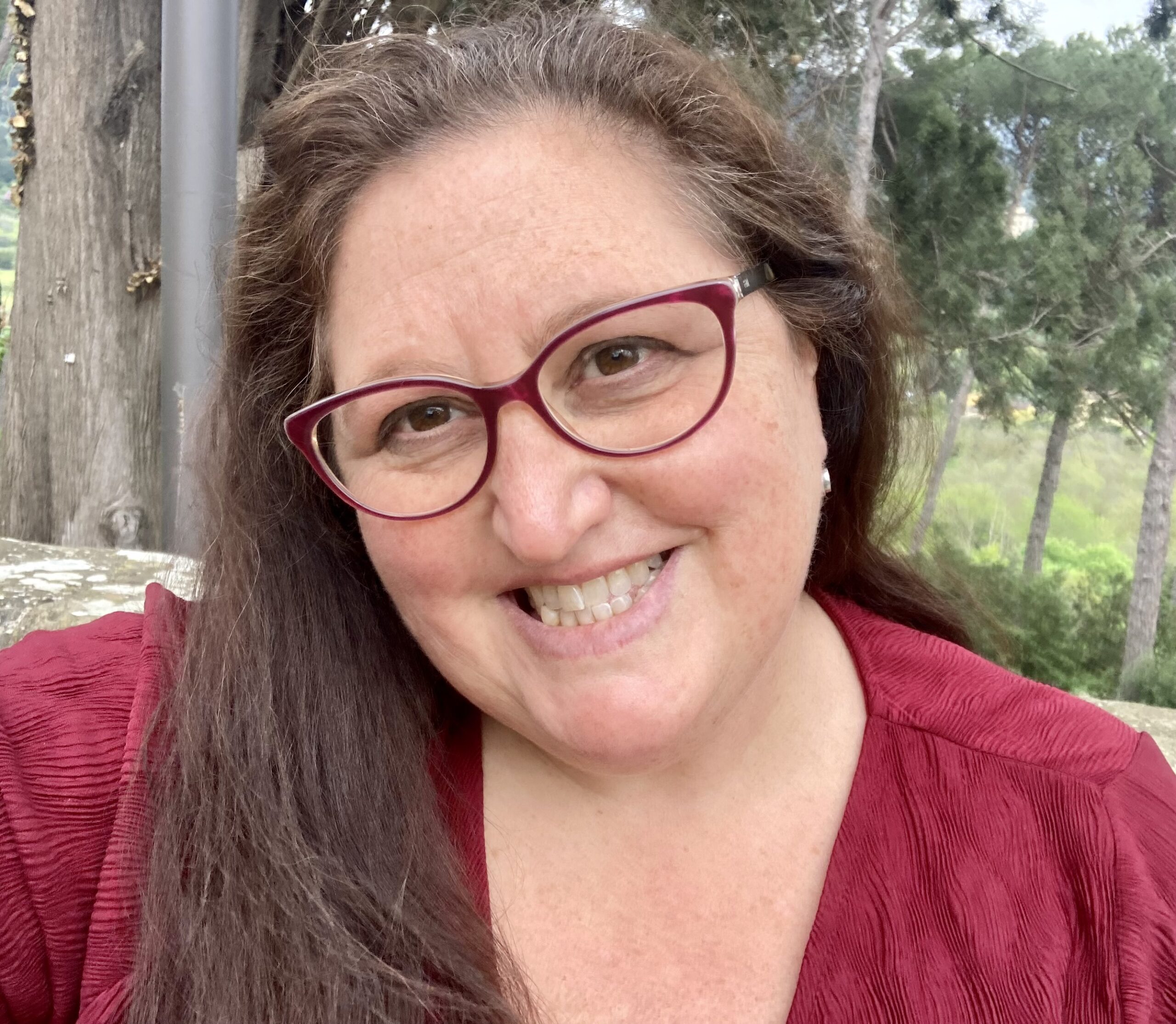 A white woman with long dark hair and glasses smiles at the camera