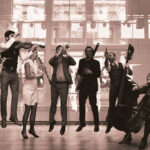 In a sepia-toned photos, a group of seven musicians with instruments