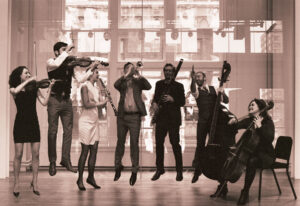 In a sepia-toned photos, a group of seven musicians with instruments