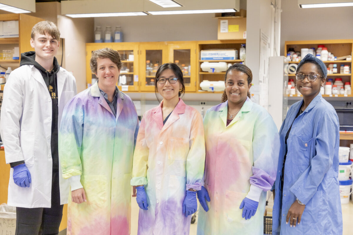 group photo of five scientists in a lab; three wearing tie-dye lab coats, one white and one blue